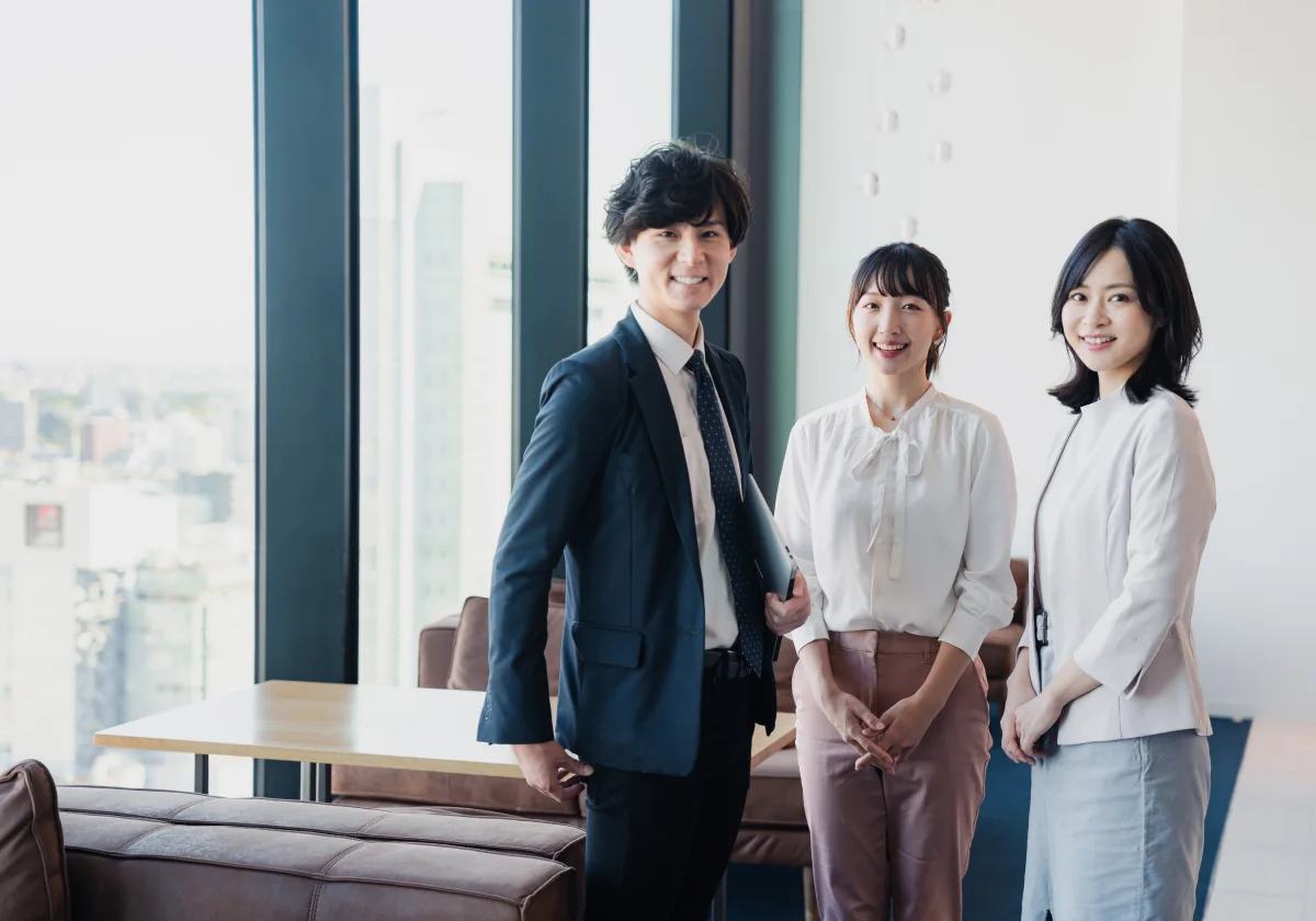 明るいオフィスで笑顔の3人のビジネスパーソンが立っている様子